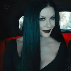 a woman with long black hair and red lipstick in a car looking at the camera