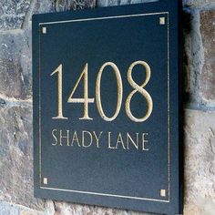 a sign that reads shady lane on it next to a stone wall with gold lettering