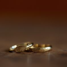 two gold wedding rings sitting on top of a wooden table with fingerprints in the middle