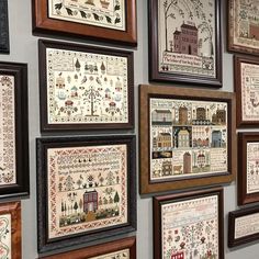 many framed pictures are hung on the wall with cross - stitch designs in them, including houses and trees