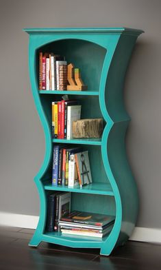 a book shelf with books on it in front of a gray wall and hardwood floor