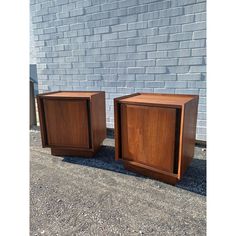 two wooden boxes sitting next to each other in front of a brick wall on gravel