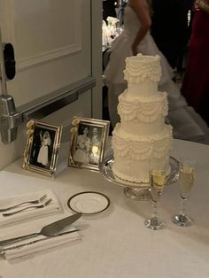 a white wedding cake sitting on top of a table next to silverware and framed pictures