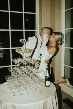 a bride and groom kissing in front of wine glasses on a table with a cake