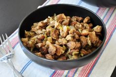 a bowl filled with stuffing sitting on top of a table next to a fork and knife