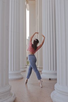 a woman standing in front of some white pillars and holding her hands up to the ceiling