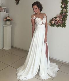 a woman standing in front of a wall wearing a white dress with flowers on it