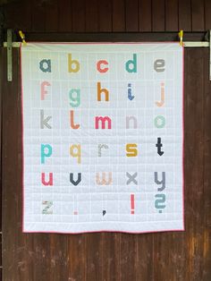 a quilted alphabet wall hanging on the side of a wooden building with an ironing board attached to it