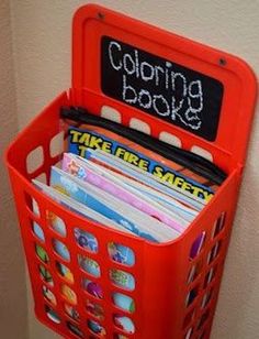 a red plastic basket holding books and folders with writing on the side that says coloring book