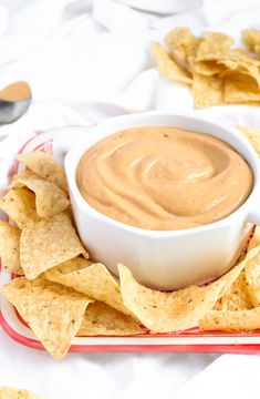 a bowl of dip surrounded by tortilla chips on a red and white plate