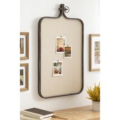 a mirror with pictures hanging on the wall next to a potted plant and books