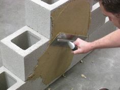 a man is using a trowel to put concrete into a block wall that's being built