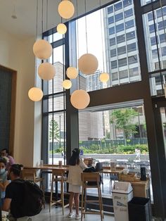 people are sitting at tables in a large room with many lights hanging from the ceiling