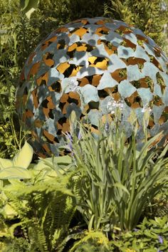 a large metal ball in the middle of some plants