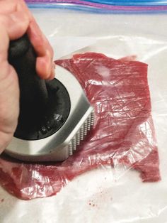 a person using a brush to cut up meat on a piece of plastic wrapping paper