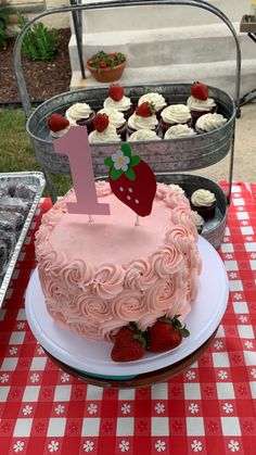 a pink frosted cake sitting on top of a table next to cupcakes