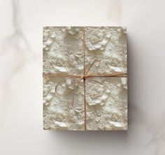 a gift box wrapped in white paper and tied with a brown ribbon on a marble surface