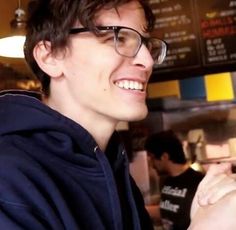 a young man wearing glasses is smiling at the camera while he holds his cell phone up to his ear