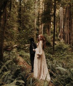 a bride and groom walking through the woods together in their wedding gowns with long sleeves