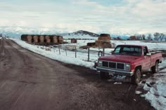 a red pick up truck parked on the side of a road next to hay bales