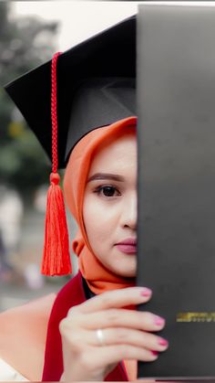 a woman wearing a graduation cap and gown holding a laptop in front of her face