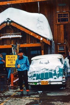 two men standing in front of a car with skis on the roof and holding signs