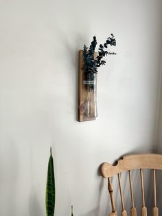 a wooden chair sitting next to a vase with flowers in it on a white wall