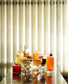 a table topped with glasses filled with different types of drinks next to a window covered in curtains