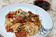 a white plate topped with pasta covered in sauce and parmesan cheese next to a glass of red wine