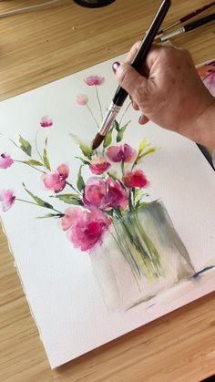 a person is painting flowers in a vase with watercolors on the paper and using a brush