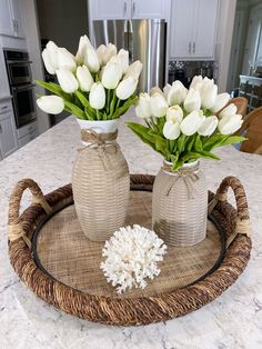 two vases with flowers in them sitting on a counter top next to a basket