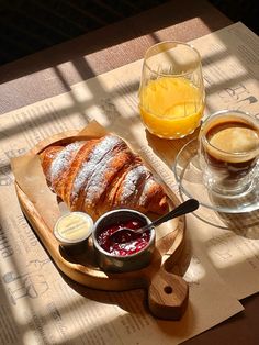 bread, jams and orange juice are sitting on a wooden tray next to a glass of orange juice