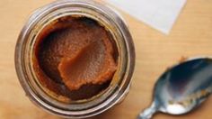 a jar filled with peanut butter sitting on top of a wooden table next to a spoon