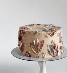 a pink cake with gold leaf decorations on top is sitting on a silver platter