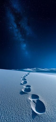 a long line of footprints in the snow under a night sky with stars and milky