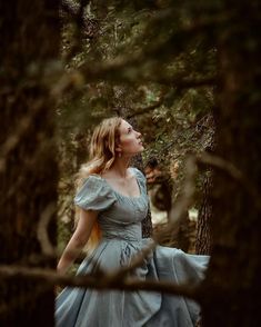 a woman in a blue dress is walking through the woods