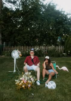 two people sitting on lawn chairs in front of a garden with flamingos and flowers