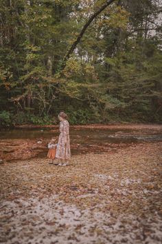 a mother and her child are standing in the middle of a forest with leaves on the ground