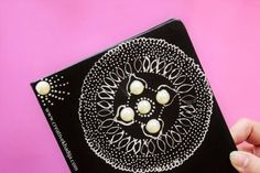 a hand holding a black and white book with pearls on it