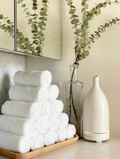 white towels are stacked on a tray next to a vase with flowers and a mirror in the background