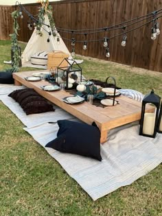 a picnic table set up with an umbrella and pillows on the grass in front of a teepee tent