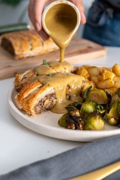 someone is pouring sauce over some food on a plate with potatoes and brussel sprouts