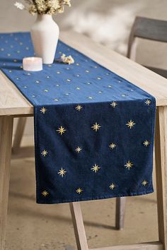 a blue table runner with gold stars on it and a white vase filled with flowers