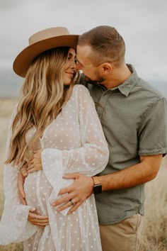 a pregnant couple cuddles in the middle of a field