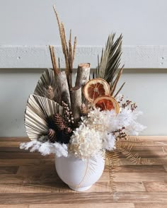 a white vase filled with lots of different types of flowers and branches on top of a wooden floor