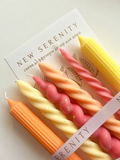 four candles with different colors and sizes are on a white surface next to a card that says new serenity