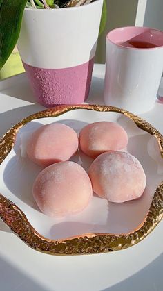 four pink donuts on a white plate next to two cups and a potted plant