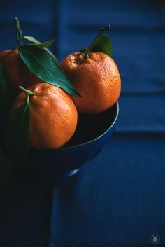 three oranges with leaves in a blue bowl