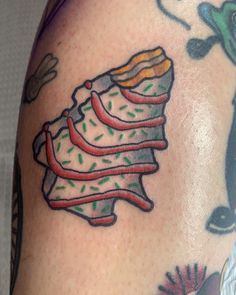 a close up of a person's arm with tattoos on it and a piece of cake in the shape of a christmas tree