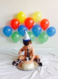 a young boy sitting on top of a bed in front of a birthday cake and balloons